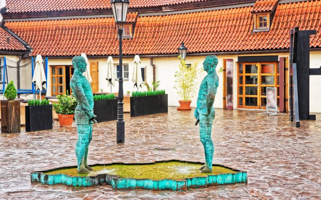 Dwie brązowe rzeźby sikających mężczyzn Davida Černého na dziedzińcu przy Muzeum Kafki w Pradze