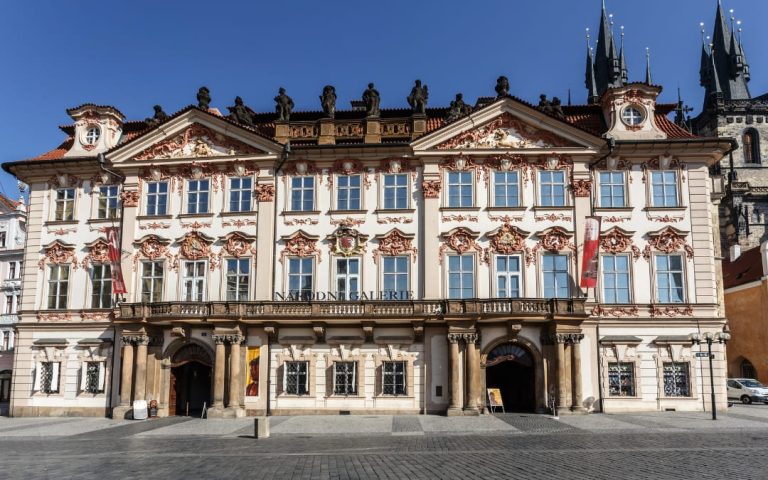 Frontalna fasada Pałacu Kinskich z napisem Národní Galerie i kościołem Najświętszej Marii Panny przed Tynem w tle