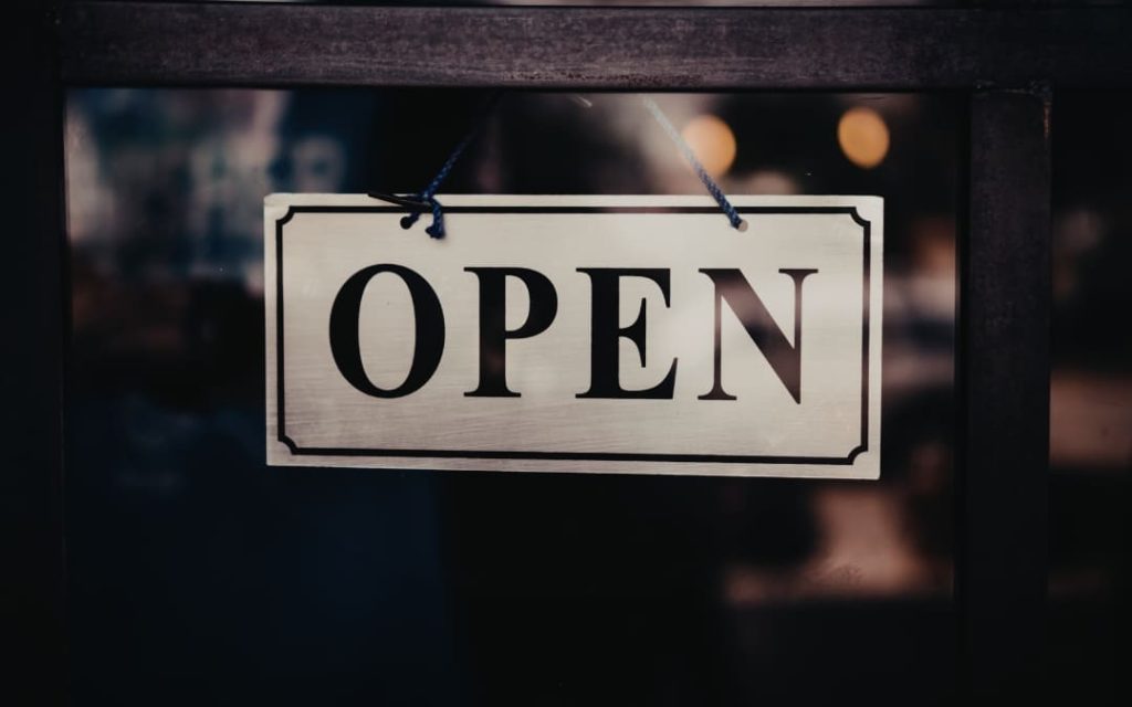 Jasna tabliczka z napisem Open zawieszona na sznurku w ciemnych drzwiach lokalu