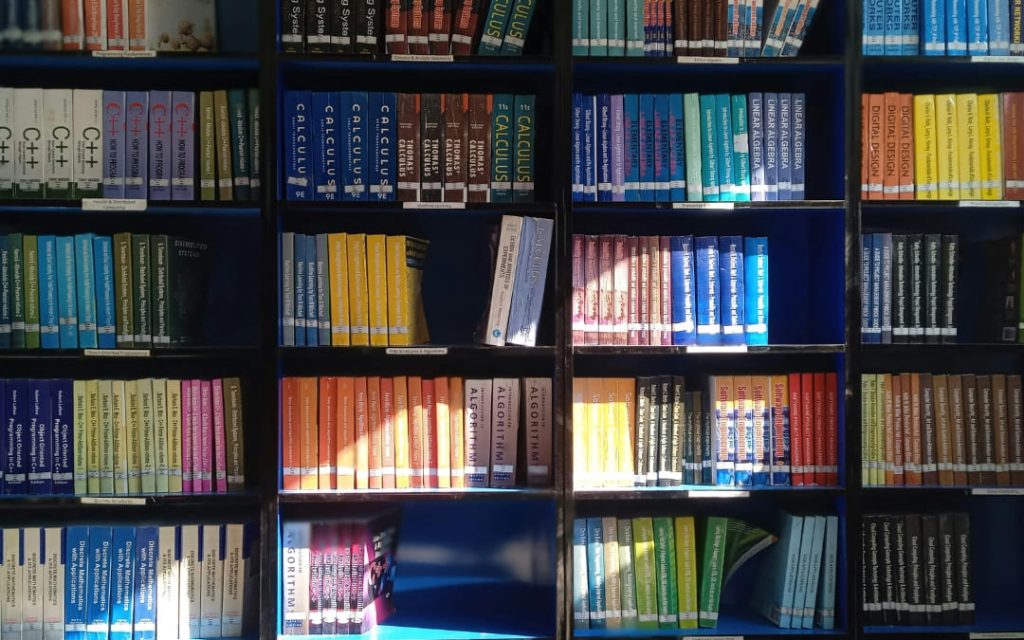 Kolorowe regały wypełnione podręcznikami akademickimi z dziedziny matematyki i informatyki w bibliotece