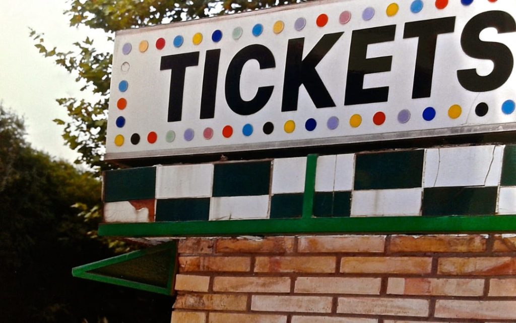 Kolorowy szyld z napisem Tickets ozdobionym wielobarwnymi kropkami na ceglianym kiosku biletowym