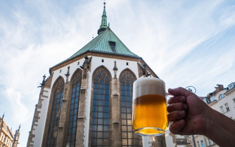 Kufel czeskiego piwa z pianką trzymany na tle gotyckiego kościoła w Pradze