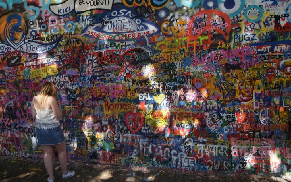 Młoda kobieta stojąca przed kolorową Ścianą Johna Lennona pokrytą graffiti w Pradze