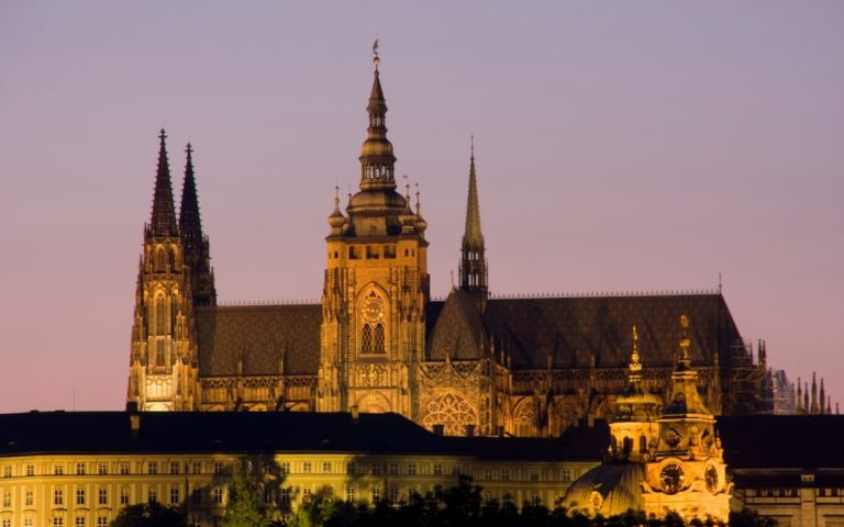 Nocna panorama Zamku Praskiego i Katedry św. Wita podświetlonych na fioletowym niebie