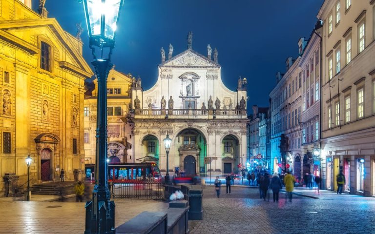 Nocna panorama kościoła Najświętszego Zbawiciela przy Klementinum w Pradze z tramwajem i przechodniami