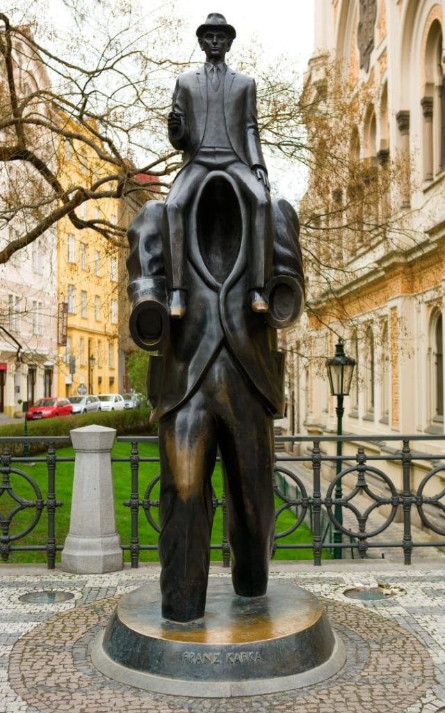 Surrealistyczna brązowa rzeźba Franza Kafki w Pradze z siedzącą figurą na pustym garniturze