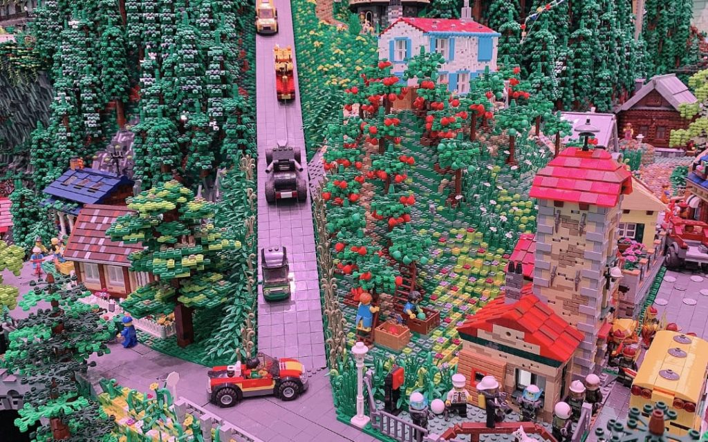 Szczegółowa makieta wiejskiej wioski z domkami, sadami i samochodami zbudowana z klocków Lego