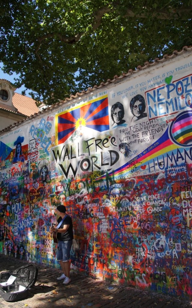 Turysta przed Ścianą Johna Lennona z napisem Wall Free World i portretem Lennona w Pradze