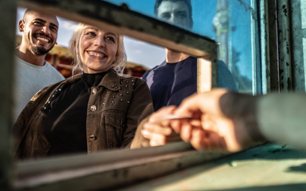 Uśmiechnięta kobieta z mężczyzną kupująca bilety w kasie przy wejściu do atrakcji turystycznej