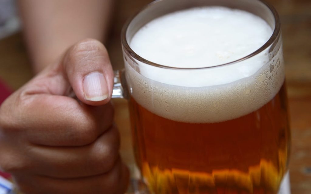 Zbliżenie na kufel czeskiego piwa z pianką trzymany w dłoni