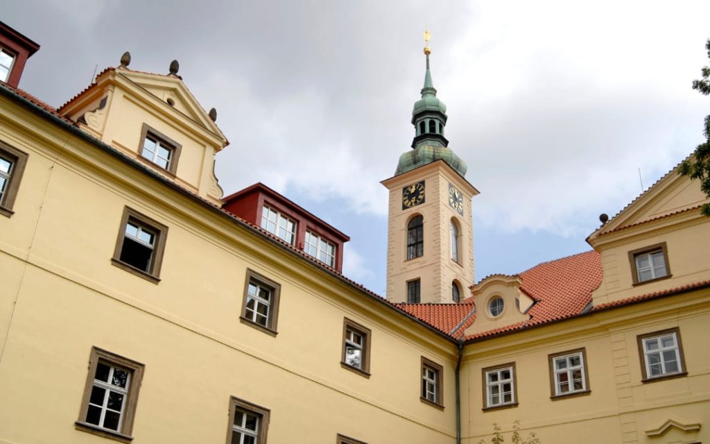 Żółta barokowa fasada dziedzińca Klementinum w Pradze z wieżą zegarową i zielonym hełmem