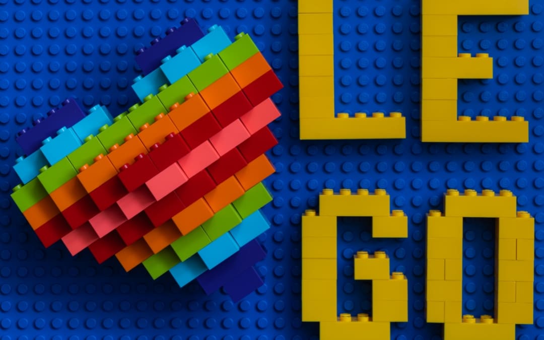 Żółty napis LEGO ułożony z klocków na niebieskiej płytce obok kolorowego serca z klocków