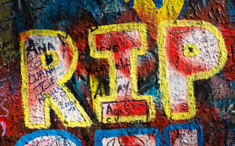 Żółty napis RIP otoczony kolorowymi graffiti i inskrypcjami na Ścianie Johna Lennona w Pradze