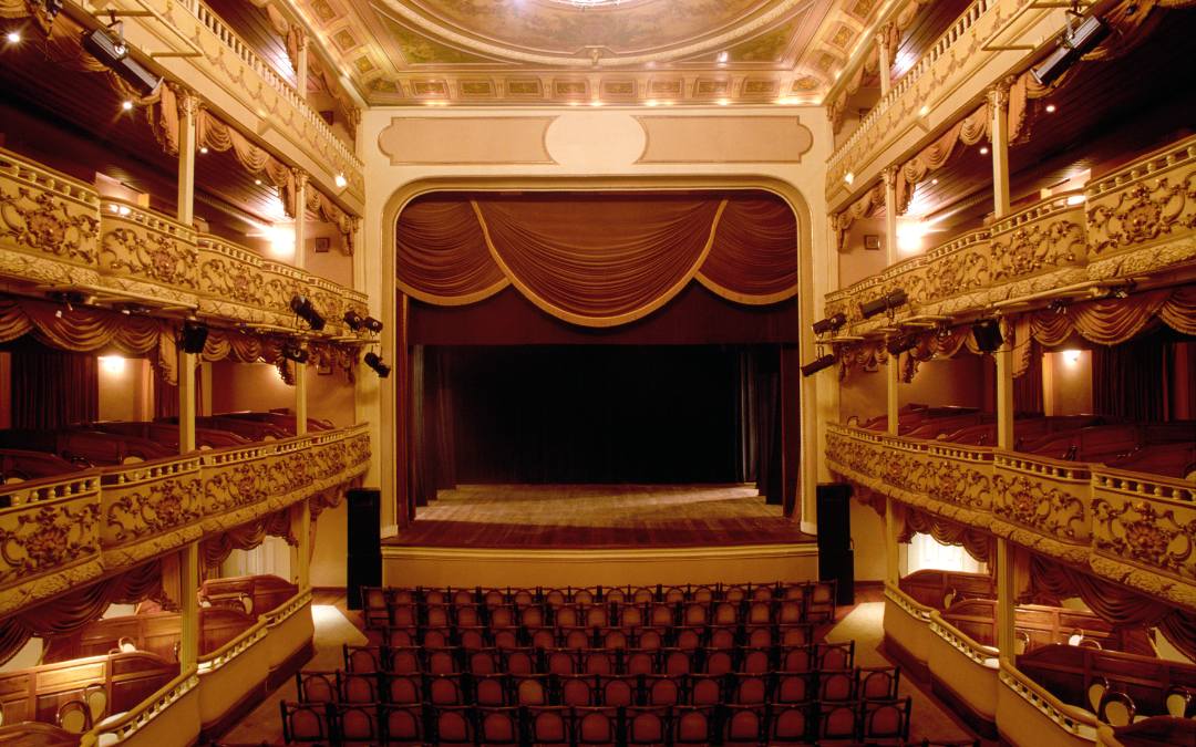 Wnętrze eleganckiego teatru z bogato zdobionymi balkonami i dużą sceną
