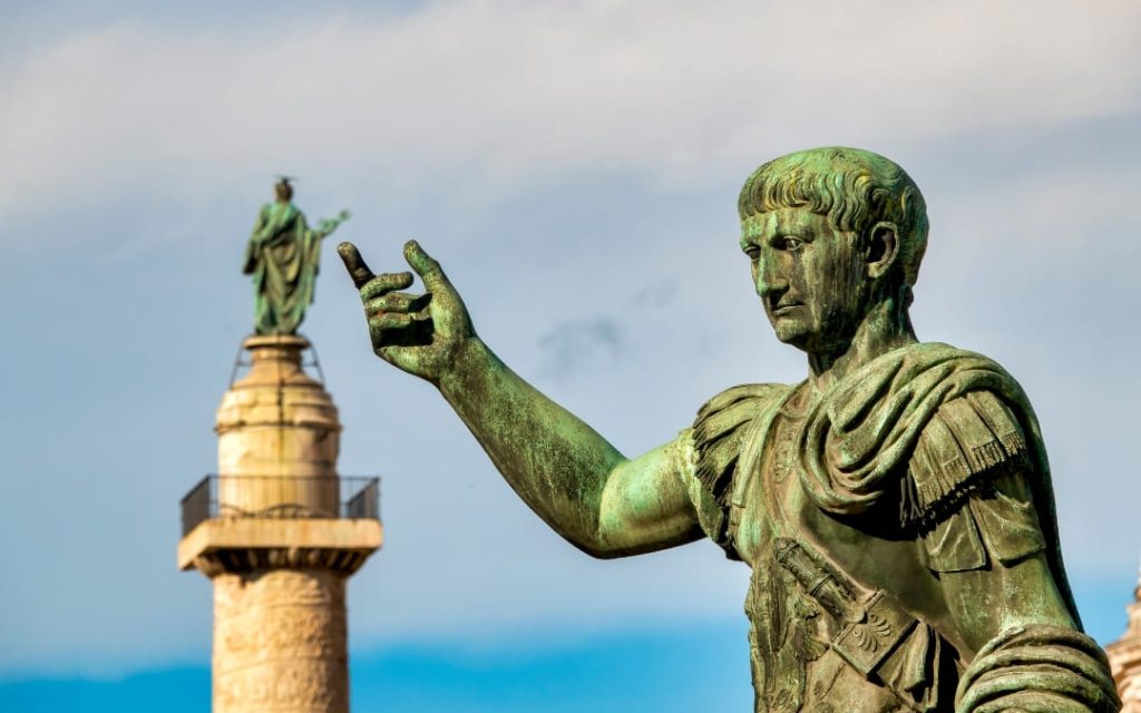 Brązowy posąg cesarza Trajana na tle Kolumny Trajana w Rzymie (Forum Trajana)