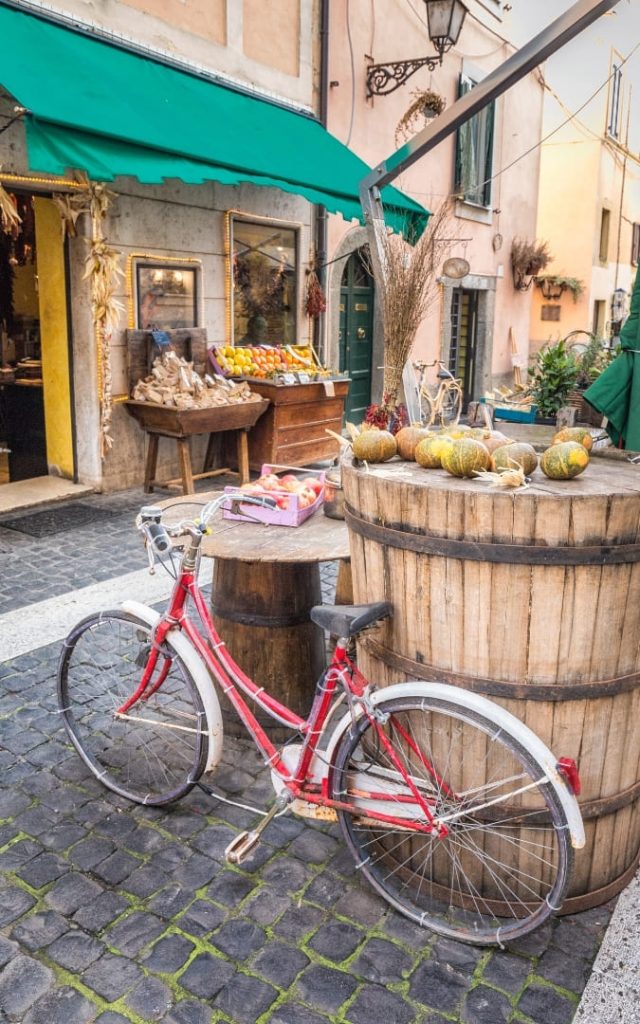 Czerwony rower i drewniane beczki z owocami przed sklepikiem w Castel Gandolfo