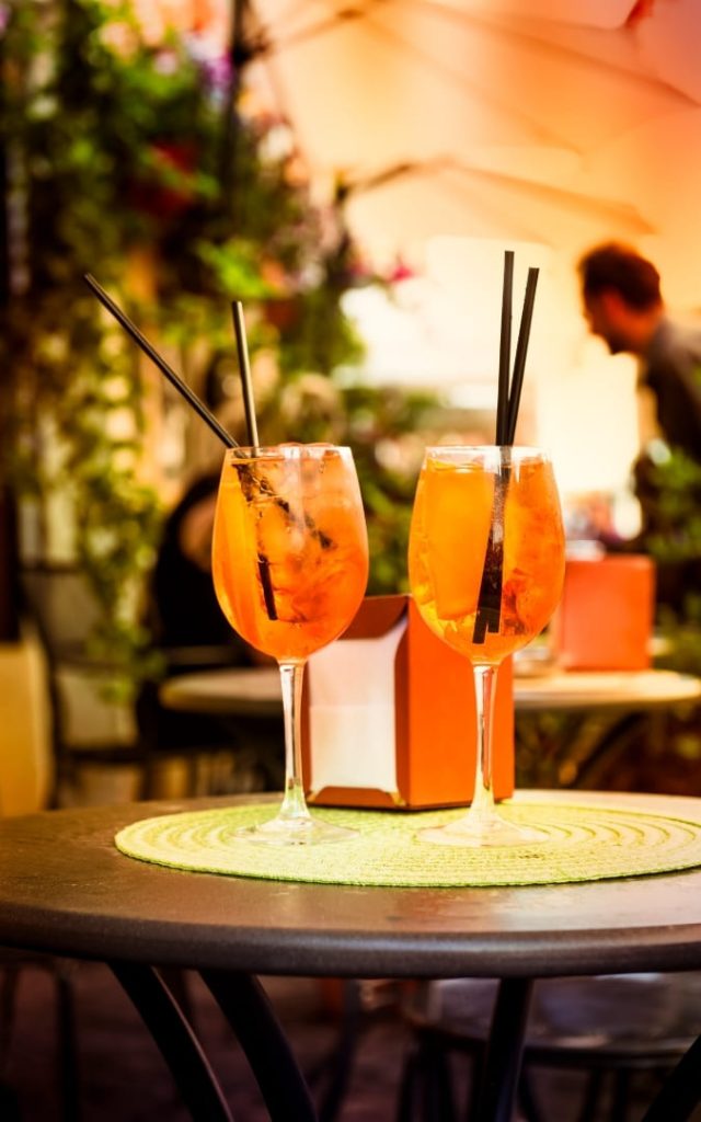 Dwa kieliszki pomarańczowego drinka Aperol Spritz na stoliku w rzymskiej kawiarni w Trastevere na świeżym powietrzu