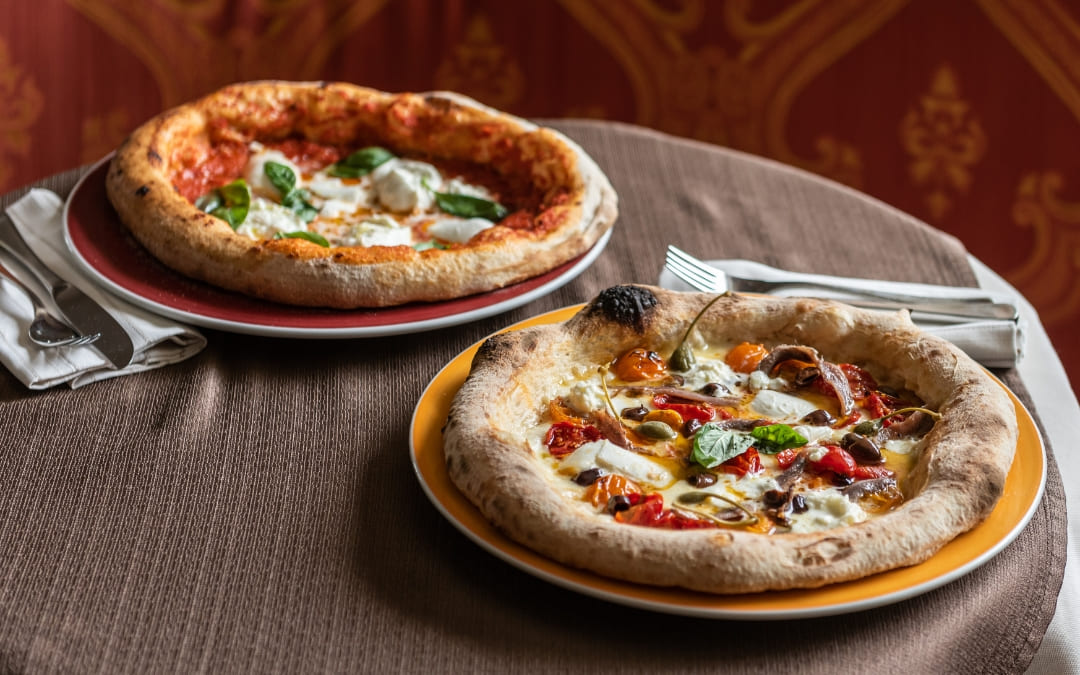 Dwie pizze neapolitańskie na grubym cieście z dodatkami serwowane na kolorowych talerzach