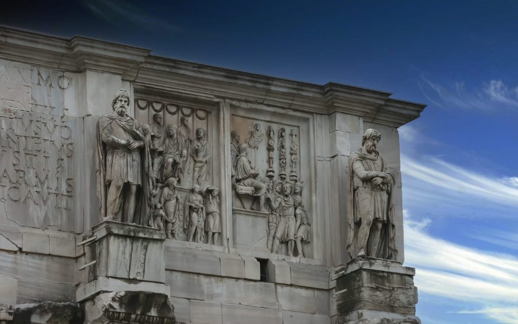 Dwie prostokątne płaskorzeźby z postaciami w togach rozdzielone rzeźbami dackich jeńców na tle błękitnego nieba