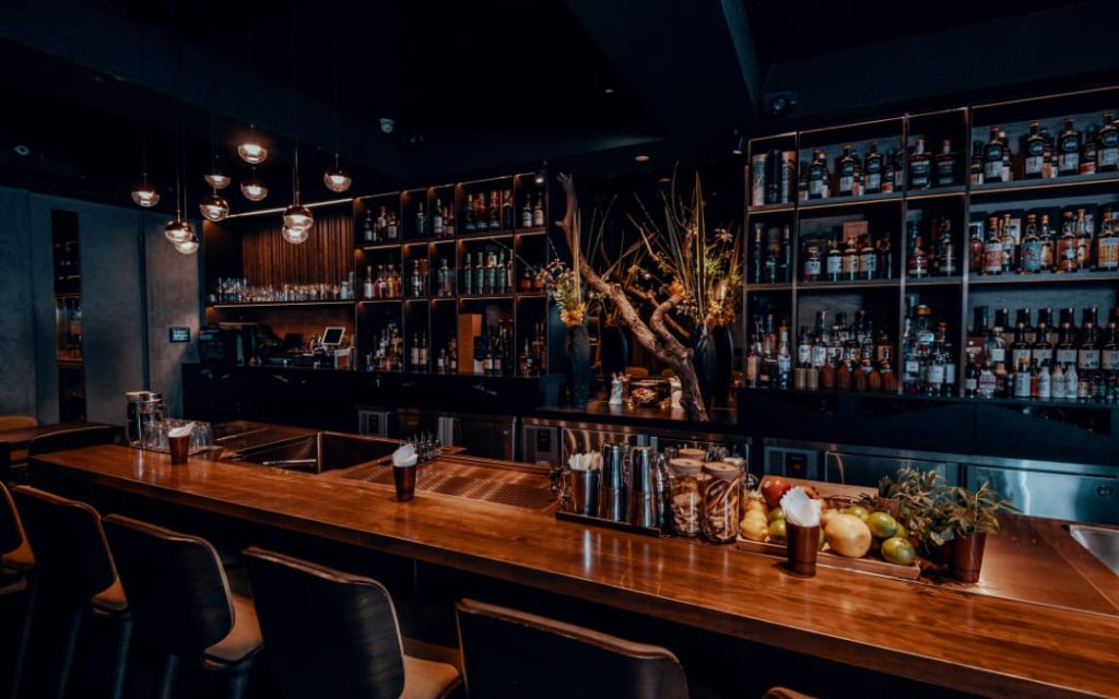 Eleganckie wnętrze nowoczesnego baru w Rzymie z długim drewnianym kontuarem i rzędami butelek alkoholu na półkach