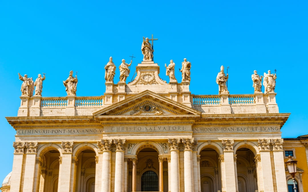 Fasada Bazyliki św. Jana na Lateranie z monumentalnymi rzeźbami świętych na tle błękitnego nieba
