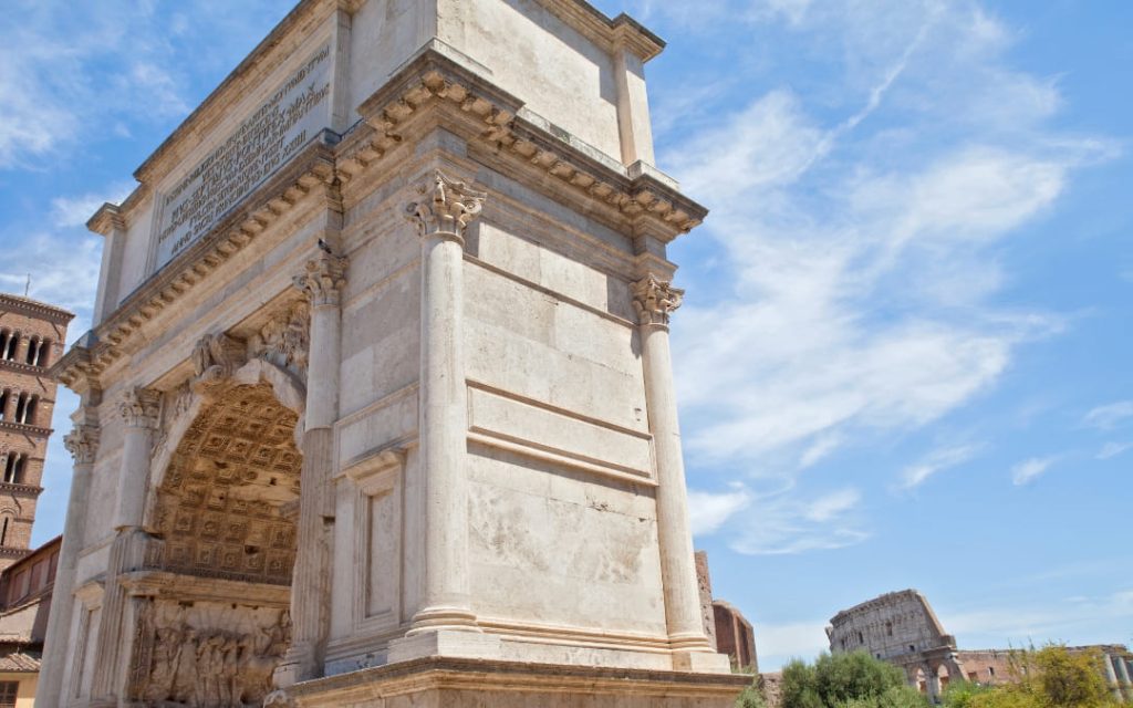 Jasny, kamienny Łuk Tytusa z widocznym w oddali Koloseum i wieżą kościoła po lewej stronie