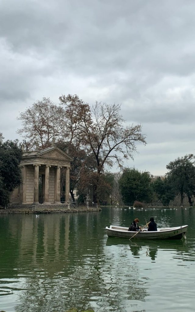 Klasycystyczna Świątynia Asklepiosa na wyspie na jeziorze w parku Villa Borghese w Rzymie z łodzią wiosłową na pierwszym planie