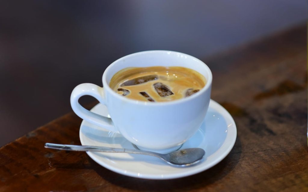 Klasyczne włoskie espresso z kostkami lodu w białej filiżance na drewnianym blacie