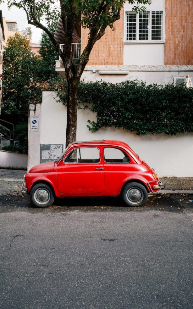 Klasyczny czerwony Fiat 500 na rzymskiej uliczce przy białym murze