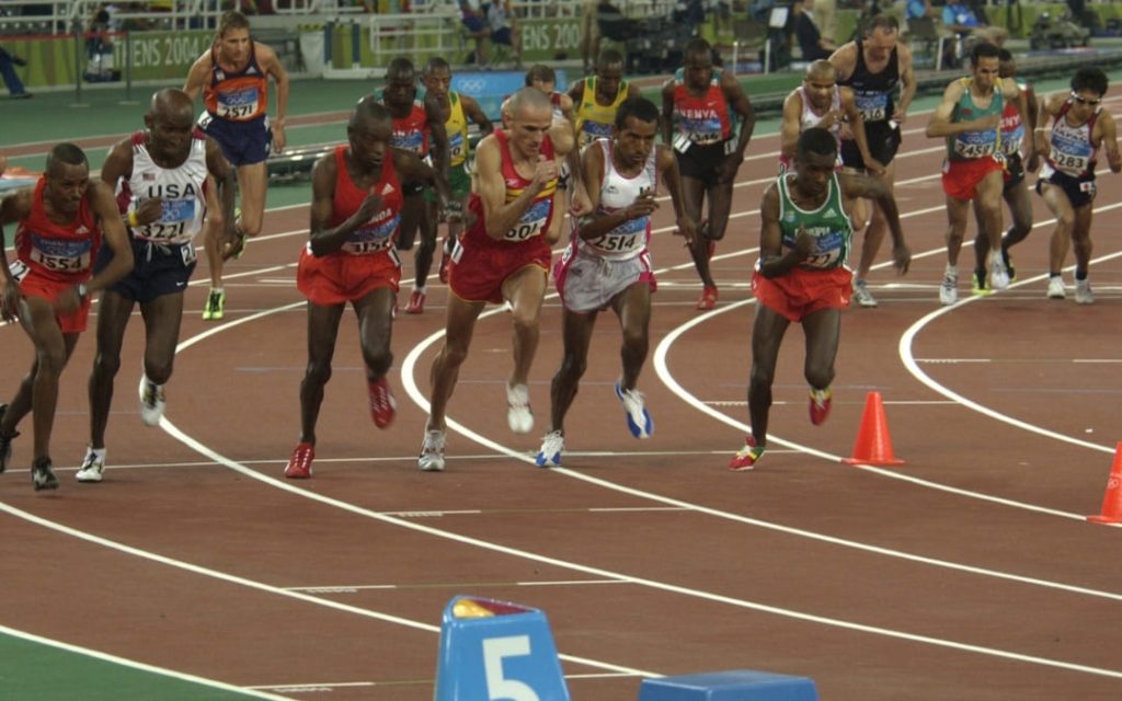 Międzynarodowa grupa lekkoatletów rozpoczynająca bieg długodystansowy na bieżni olimpijskiej