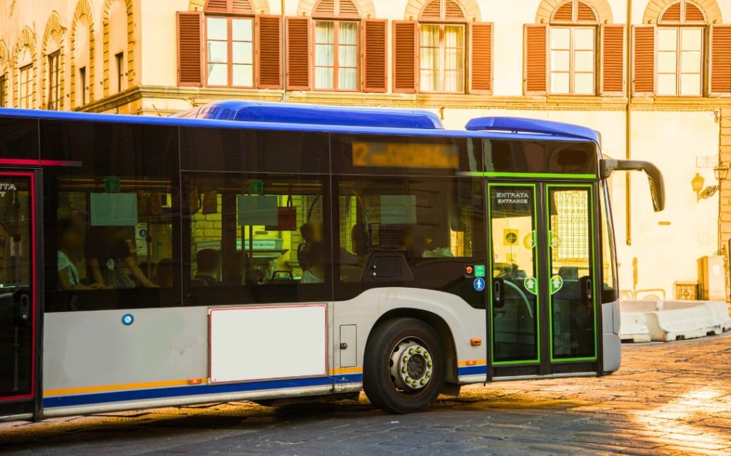 Nowoczesny włoski autobus miejski z niebieskim dachem stojący na przystanku obok zabytkowej kamienicy z okiennicami