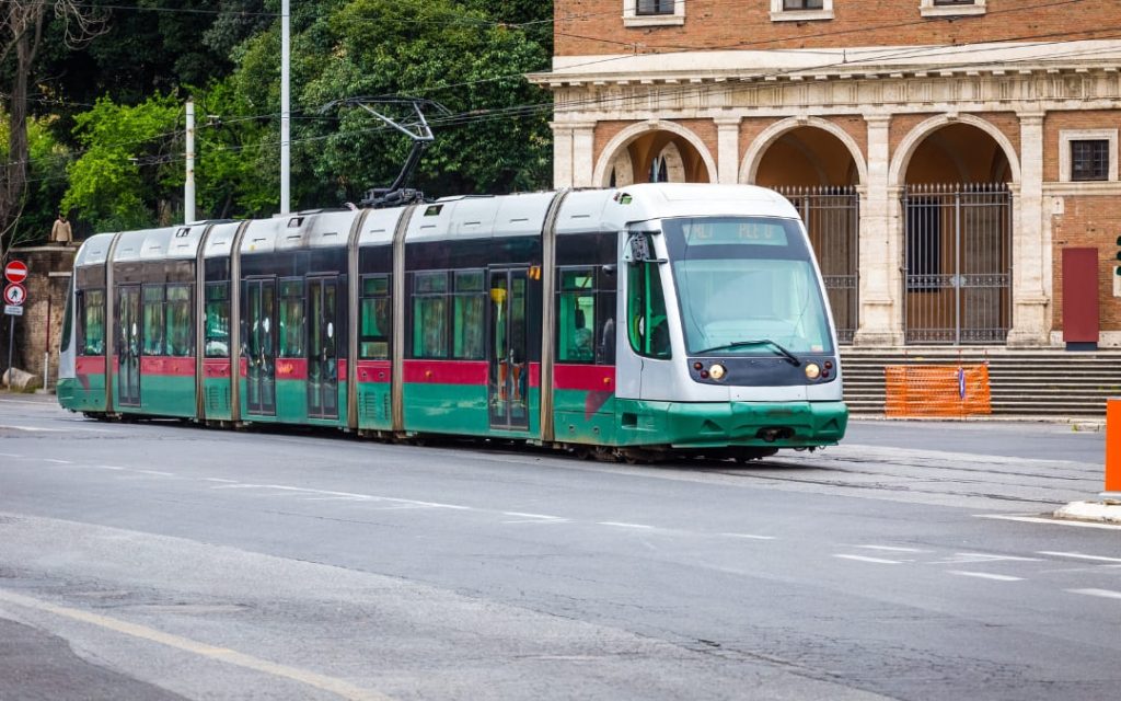 Nowoczesny zielono-szary tramwaj rzymskiej sieci ATAC jadący ulicą obok zabytkowej fasady z arkadami