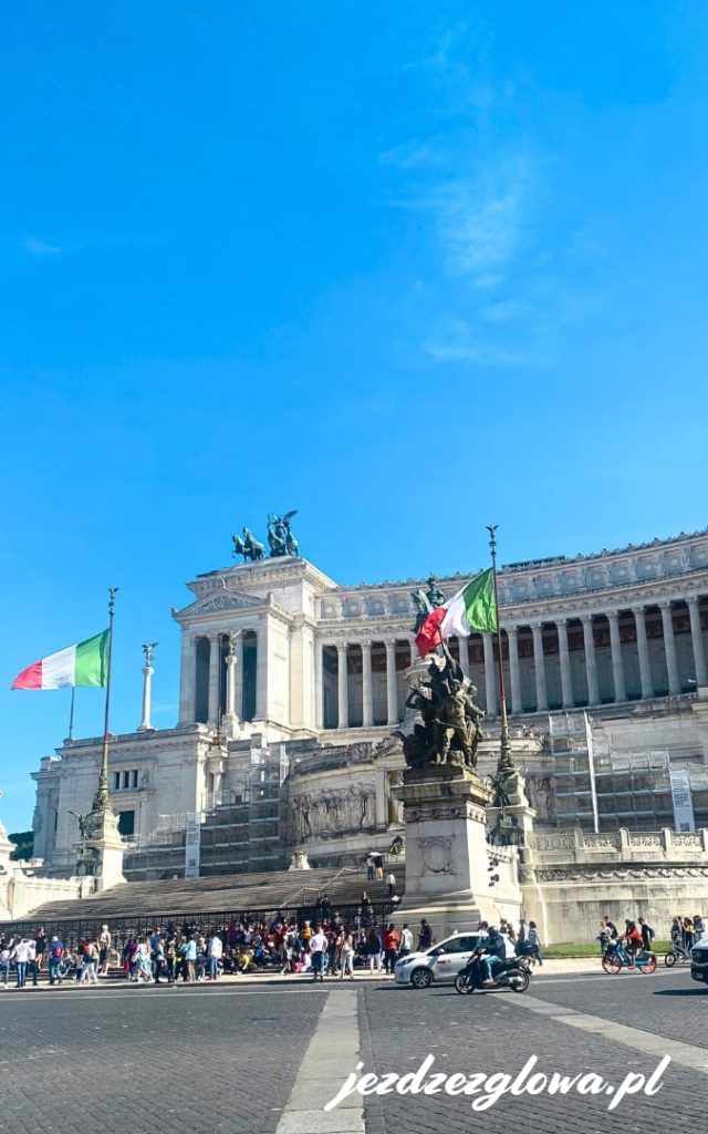 Biały marmurowy Ołtarz Ojczyzny na Piazza Venezia w Rzymie z włoskimi flagami na tle błękitnego nieba