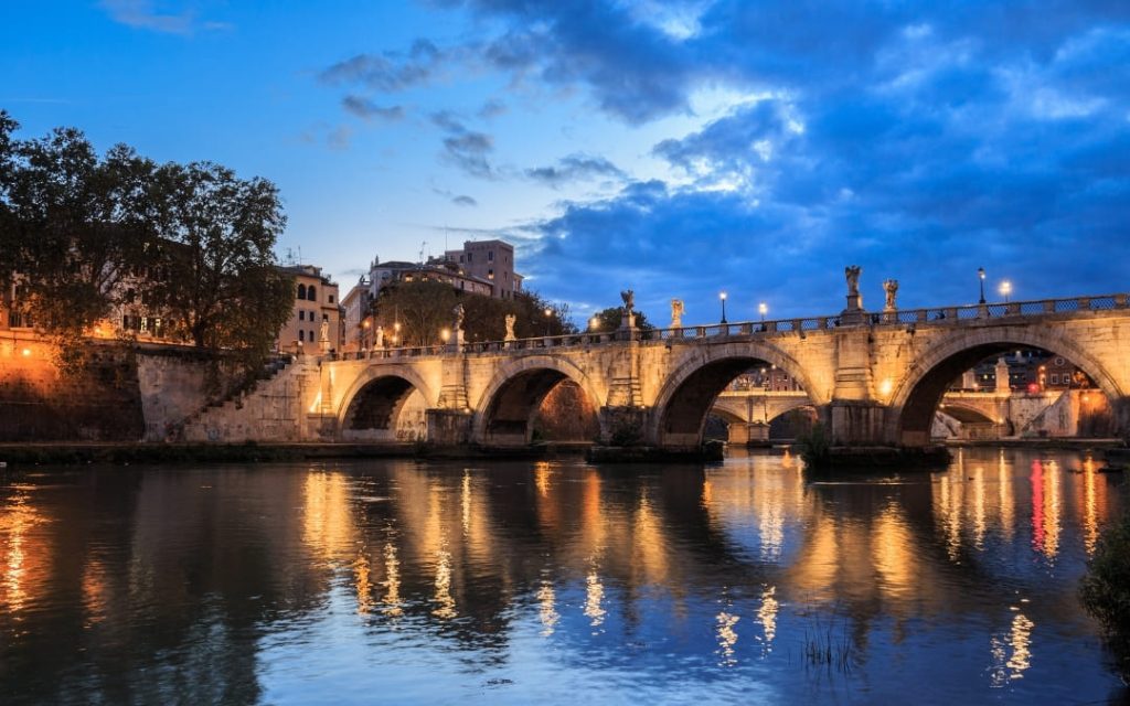 Oświetlony most Ponte Sant’Angelo nad Tybrem w Rzymie o zmierzchu
