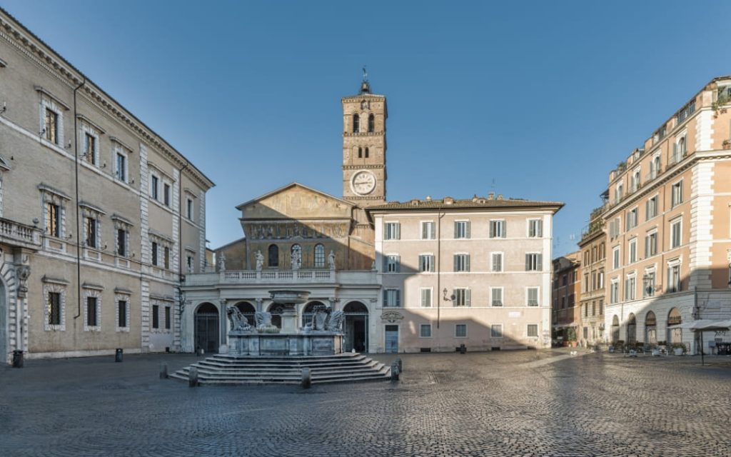 Piazza di Santa Maria in Trastevere w Rzymie z zabytkową fontanną i fasadą bazyliki w porannym świetle