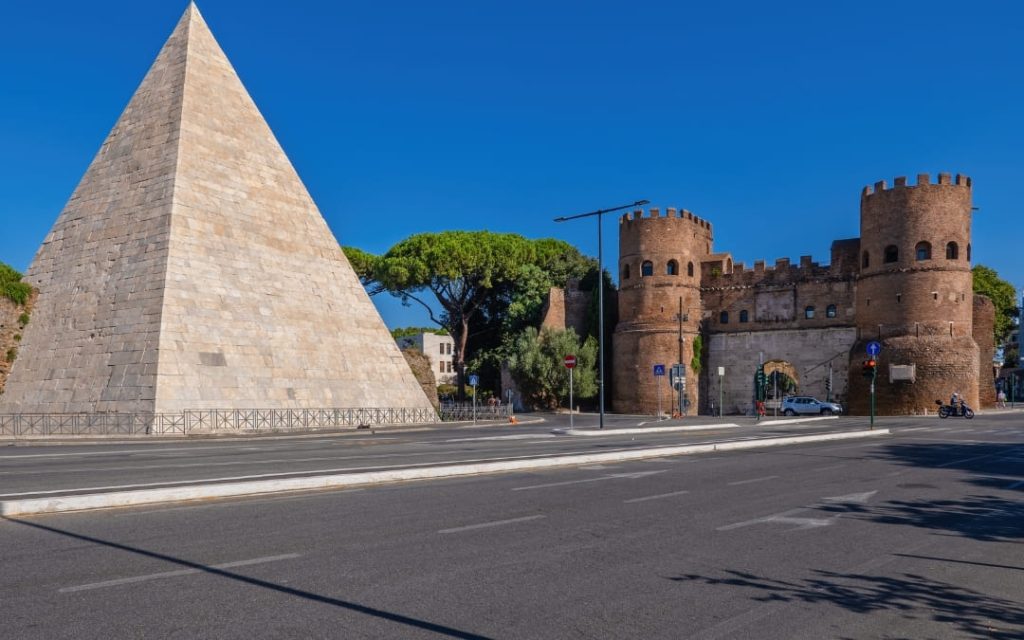 Piramida Cestiusza i brama Porta San Paolo w Rzymie przy pustej ulicy w pełnym słońcu