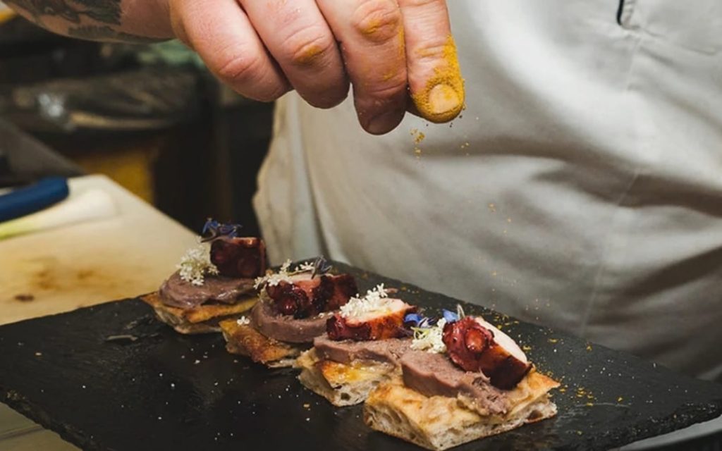 Pizza al taglio od Bonci Pizzarium z ośmiornicą i jadalnymi kwiatami na kamiennej płycie