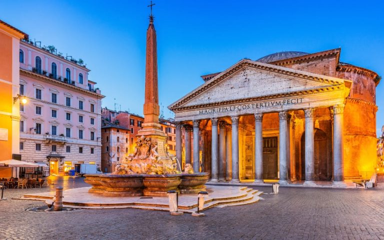 Podświetlona fasada rzymskiego Panteonu i fontanna z obeliskiem na placu Piazza della Rotonda o zmierzchu