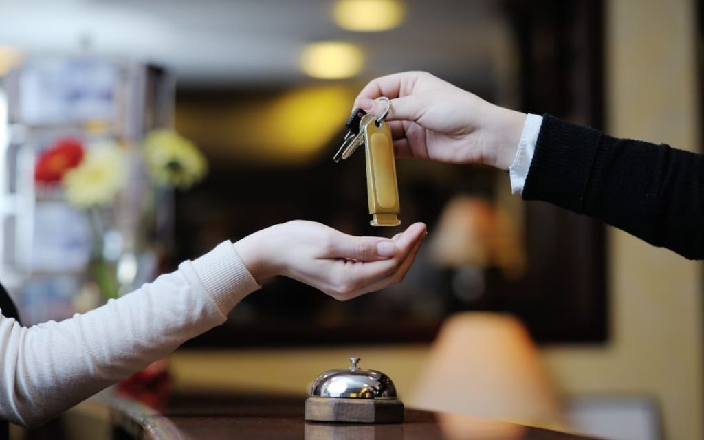 Recepcjonista przekazujący tradycyjny klucz z mosiężnym brelokiem gościowi nad ladą w hotelu