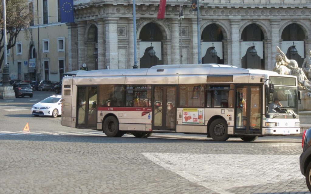 Srebrny autobus komunikacji miejskiej ATAC jadący przez rzymski plac w słoneczny dzień