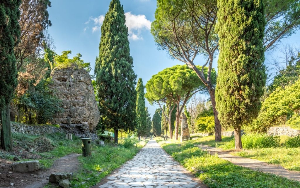 Starożytna brukowana droga Via Appia Antica w Rzymie otoczona wysokimi cyprysami i sosnami piniowymi