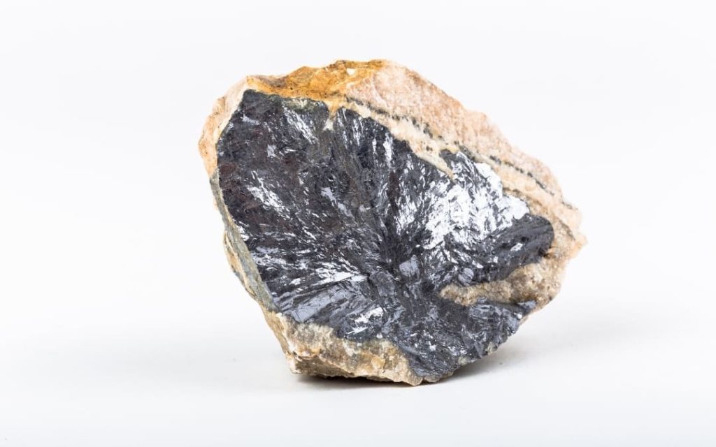 Surowa bryła ciemnoszarej, błyszczącej galeny osadzona w jasnej skale na białym tle