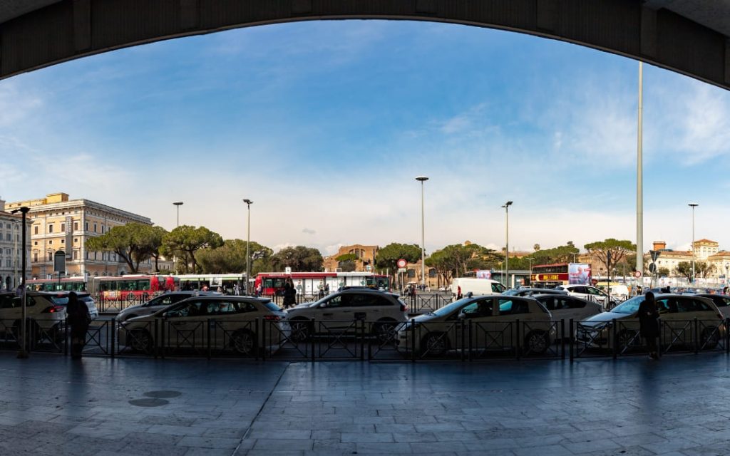 Szereg białych taksówek zaparkowanych przed dworcem Roma Termini w słoneczny dzień