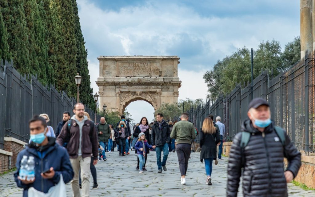 Tłum ludzi spacerujący brukowaną aleją w stronę Łuku Tytusa na rzymskim Forum Romanum