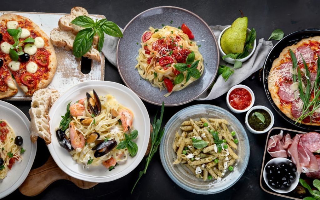 Tradycyjne dania kuchni włoskiej w tym tagliatelle z krewetkami i penne z pesto serwowane na ciemnym blacie