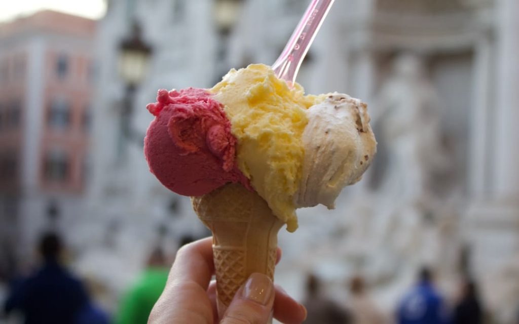 Tradycyjne włoskie lody gelato w wafelku z trzema gałkami trzymane przed Fontanną di Trevi w Rzymie