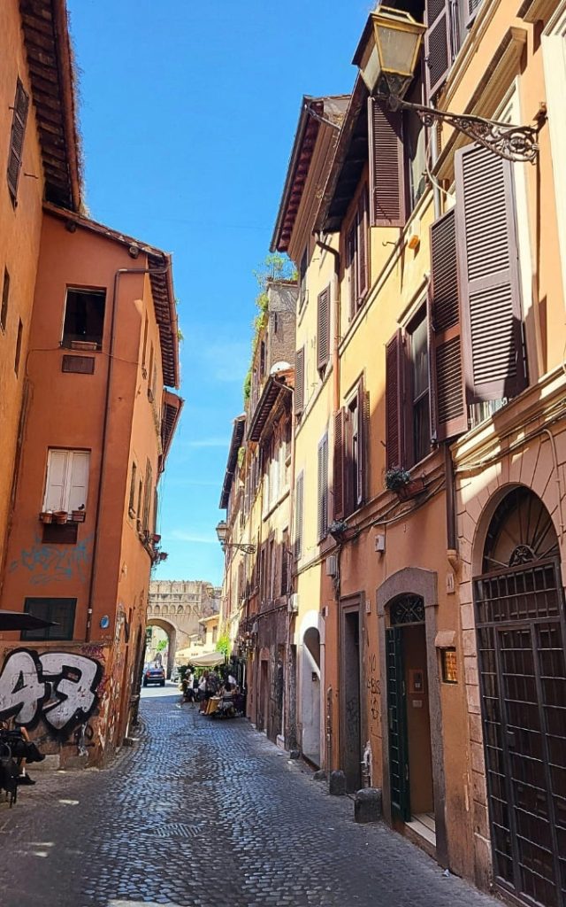 Wąska brukowana uliczka w rzymskiej dzielnicy Trastevere z wysokimi kamienicami w odcieniach ochry i pomarańczy