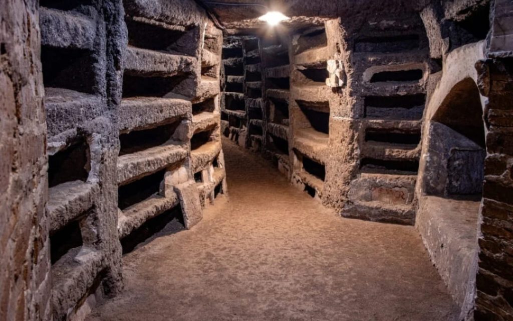 Wąski podziemny korytarz w Katakumbach Pryscylli w Rzymie z licznymi niszami grzebalnymi typu loculi wykutymi w skale