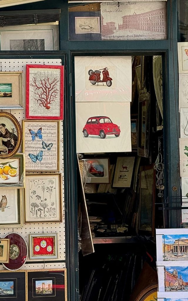 Witryna rzymskiego sklepu z pamiątkami z rysunkami czerwonego Fiata 500 i skutera Vespa na papierze