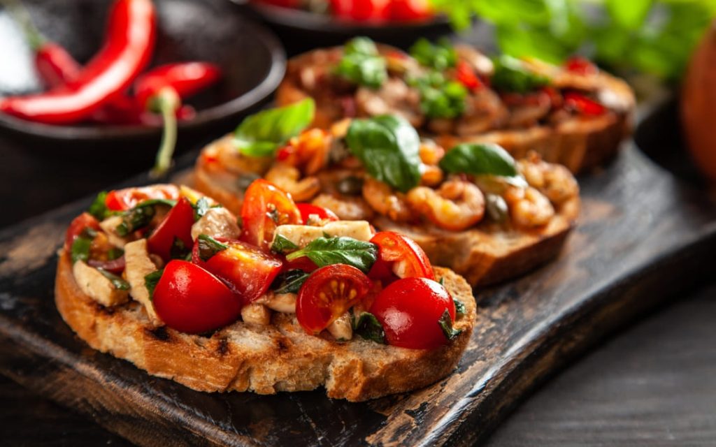 Włoska bruschetta z pomidorkami koktajlowymi bazylią i czosnkiem na drewnianej desce